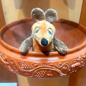 Das Bild zeigt die Maus aus der Sendung mit der Maus als Plüschfigur. Die Maus sitzt in einem Reibgefäß aus Terra Sigillata.