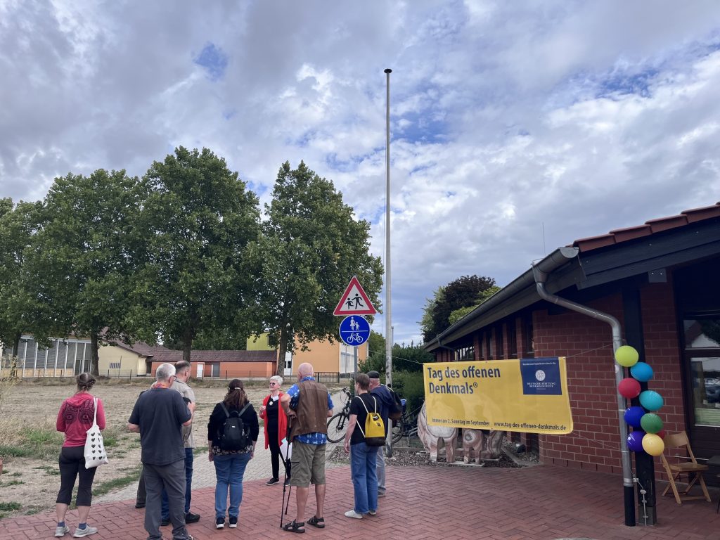 Besuchergruppe ToffD 2026 eine Besuchergruppe steht vor dem Schutzbau der römischen Brennöfen in Rheinzabern. Sie wenden sich der unter der Wiese liegenden Römerstraße zu.